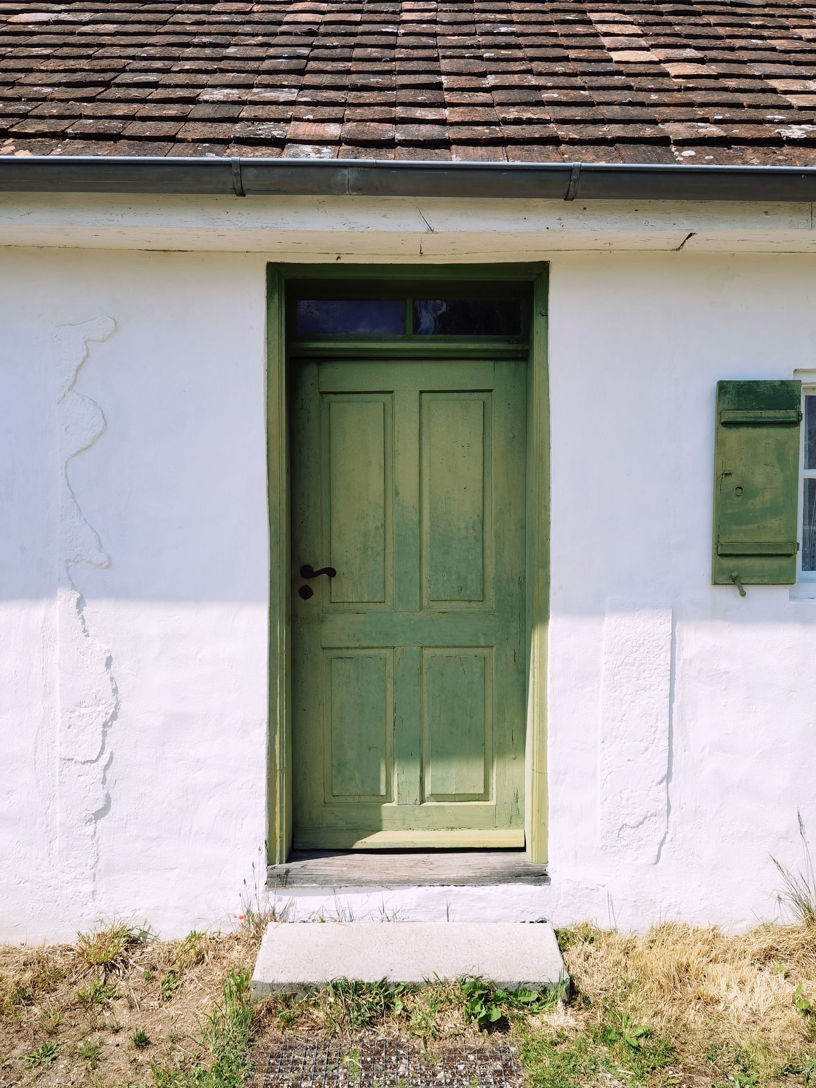 A sage green composite back door on a white cottage wall